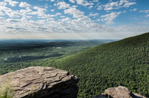 A panoramic view of lush green mountains under a partly cloudy sky, with a rocky foreground.