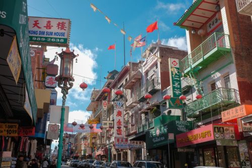 Colorful street scene in Chinatown with shops, lanterns, and flags under a bright blue sky.