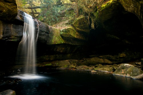 A serene waterfall cascades into a tranquil pool, surrounded by lush greenery and rocky cliffs.