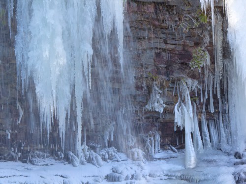 Icicles hang from a rocky surface, with frozen water cascading down, creating a wintery, icy landscape.