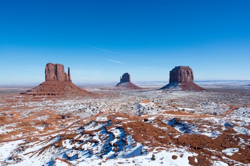 Snow-covered landscape featuring iconic red rock formations under a clear blue sky.
