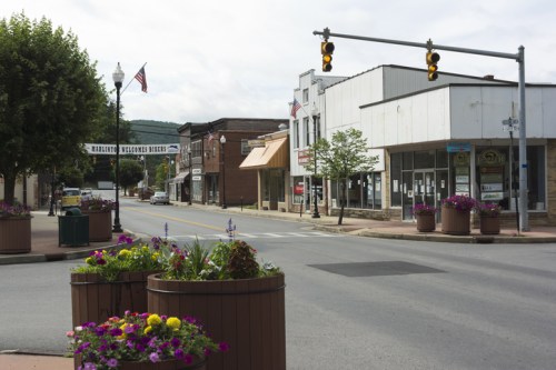 A quiet street scene featuring shops, planters with flowers, and traffic lights under a cloudy sky.