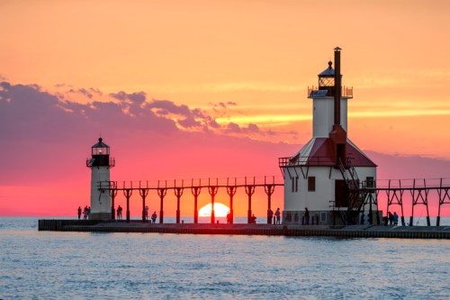 A picturesque sunset over a pier with two lighthouses, silhouetted against vibrant orange and pink skies.