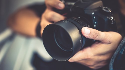 A close-up of a person holding a camera with a large lens, ready to take a photo.