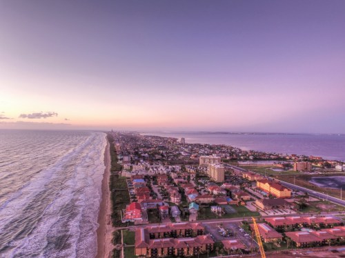 Aerial view of a coastal city at sunset, featuring the ocean, shoreline, and residential buildings along the beach.