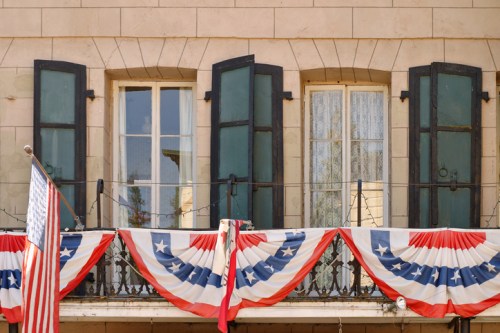 A balcony adorned with red, white, and blue bunting, featuring open windows and an American flag.