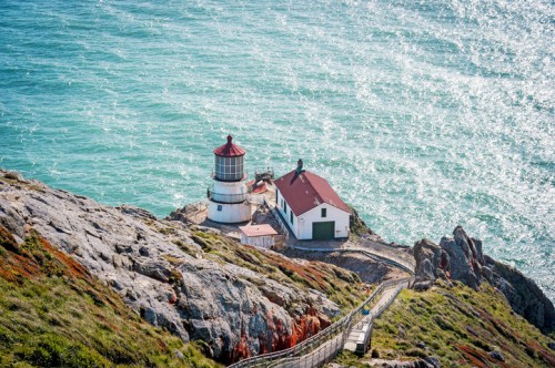 A scenic lighthouse on a rocky coastline, surrounded by turquoise waters and lush greenery.