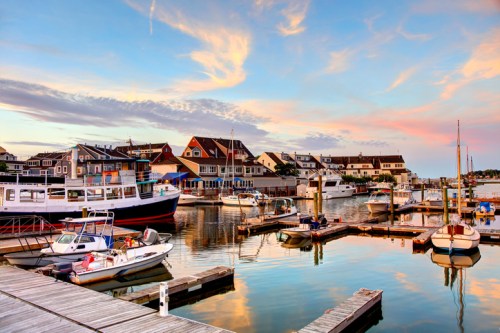 A serene marina at sunset, featuring boats docked and colorful buildings reflecting in the calm water.