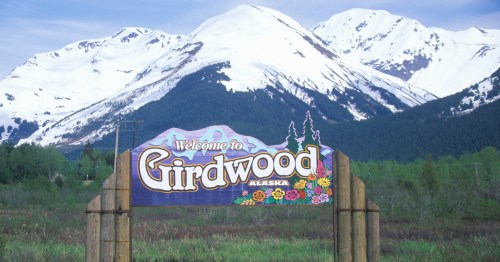 Welcome to Girdwood sign against a backdrop of snow-capped mountains and green trees.