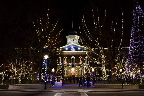 A beautifully lit building surrounded by trees adorned with colorful holiday lights at night.