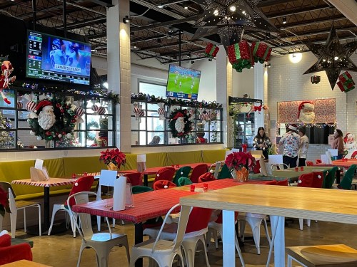 A festive restaurant decorated for the holidays, featuring Christmas lights, poinsettias, and TVs showing sports.