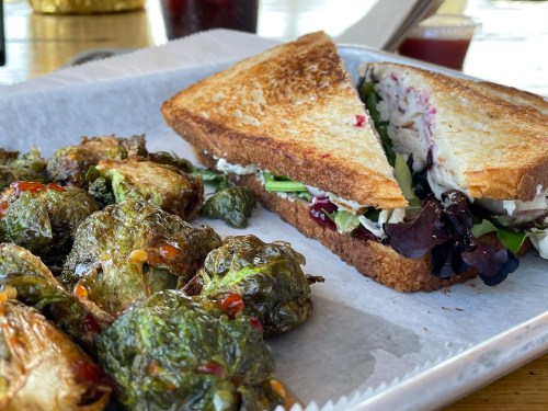 A toasted sandwich filled with greens and a side of roasted Brussels sprouts on a tray.