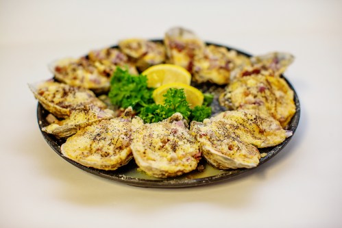 A platter of baked oysters garnished with lemon slices and parsley.