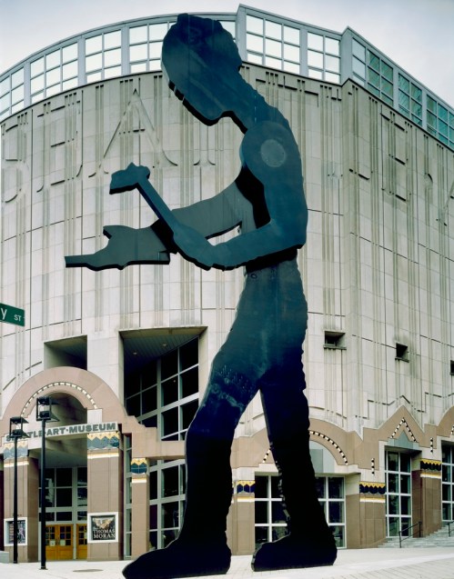 A large silhouette of a worker holding a hammer stands in front of a modern art museum building.