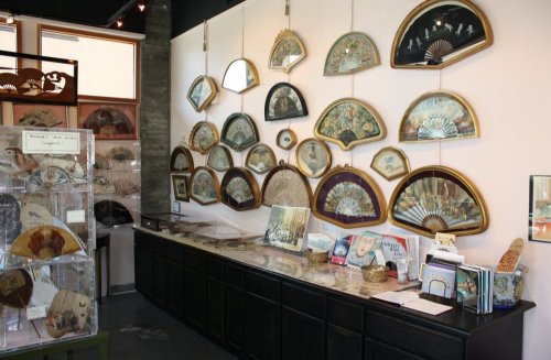 A display of decorative fans on a wall, with a counter showcasing books and additional fans in a shop setting.