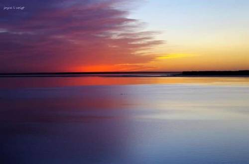 A serene sunset over calm waters, with vibrant hues of orange, pink, and purple reflecting on the surface.