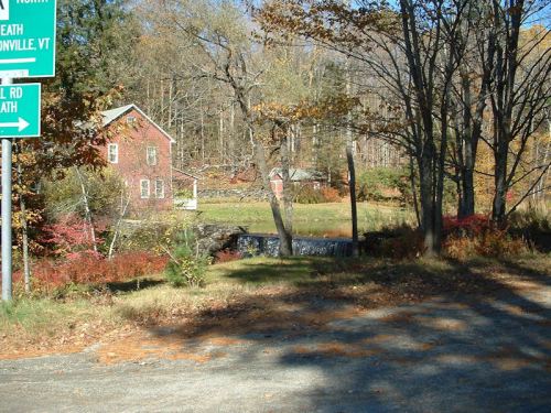 A red house surrounded by trees and autumn foliage, with a road sign indicating directions in a rural setting.