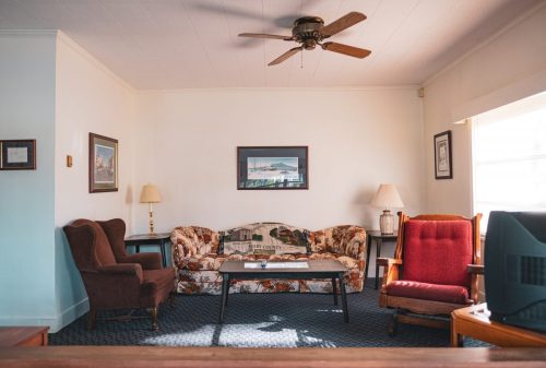 Cozy living room with a patterned couch, two armchairs, a coffee table, and a ceiling fan, illuminated by natural light.
