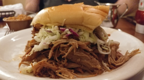A plate featuring a piled-high sandwich with pulled pork and shredded lettuce on a soft bun.