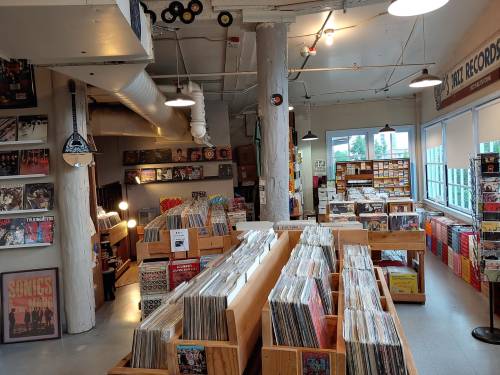 A cozy record store filled with wooden shelves of vinyl records, posters, and warm lighting.