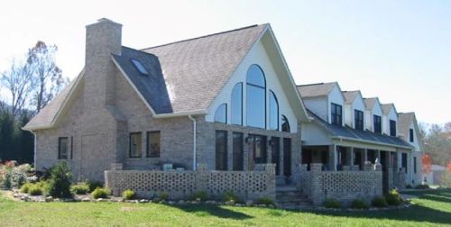 A large, modern house with a stone exterior, large windows, and a spacious porch surrounded by greenery.