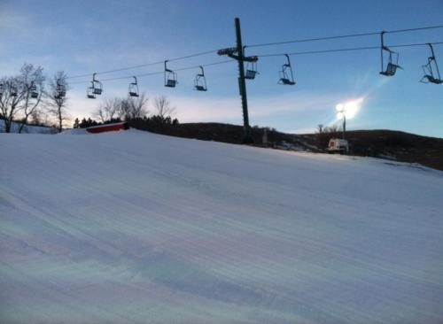 A snowy slope with ski lifts in the background under a twilight sky.