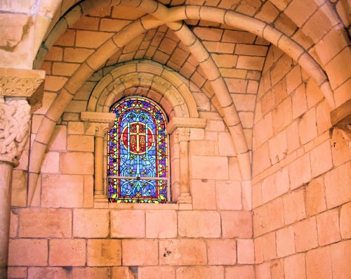 Stained glass window featuring a cross, set in a stone wall with arched architecture.