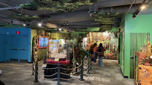 A vibrant indoor exhibit featuring lush green decor, displays, and visitors exploring the space.