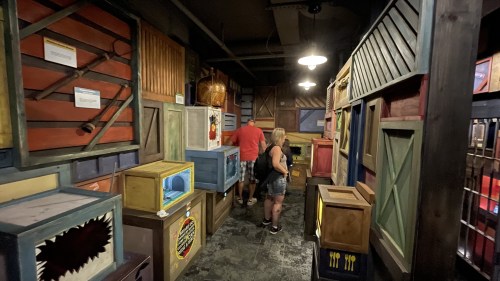 A dimly lit room filled with colorful crates and boxes, with two people exploring the space.