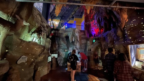 A dimly lit cave-like space with colorful lights, rock formations, and people exploring the area.