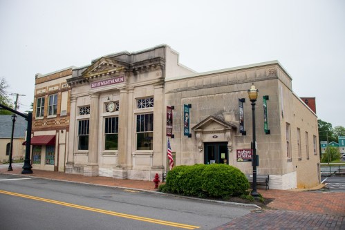 Historic building with a clock, banners, and an entrance, located on a street with greenery and a fire hydrant nearby.