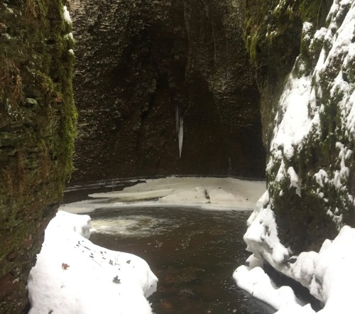 A narrow canyon with snow-covered rocks and a frozen river flowing through the center.
