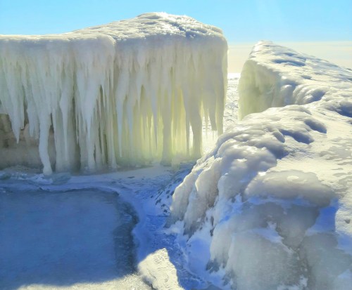 Icicles and frozen formations on a snowy landscape under a clear blue sky.