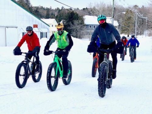 A group of cyclists riding fat bikes on a snowy path, wearing winter gear and enjoying the winter scenery.