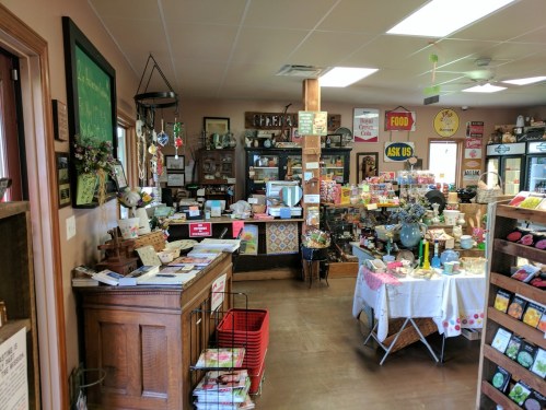 A cozy shop interior filled with various items, including gifts, food signs, and a checkout counter.