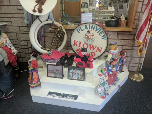 Display featuring clown memorabilia, including costumes, photos, and a sign for the Plainview Klown Band.