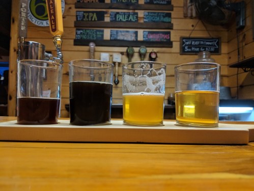 A wooden table with four glasses of different craft beers in a cozy bar setting.