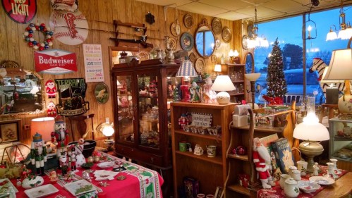 A cozy vintage shop filled with antiques, holiday decor, and warm lighting, showcasing various collectibles and decorations.