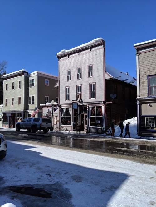 A snowy street scene featuring historic buildings and a parked truck under a clear blue sky.