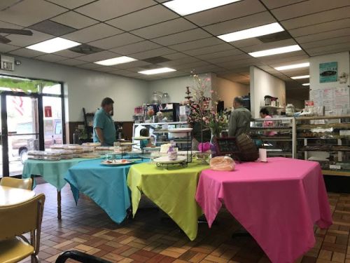 A colorful bakery interior with tables covered in pink and green cloths, displaying various baked goods.