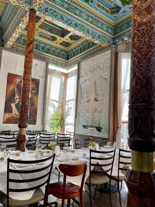 Elegant restaurant interior featuring ornate ceiling, decorative walls, and wooden pillars, set for dining.