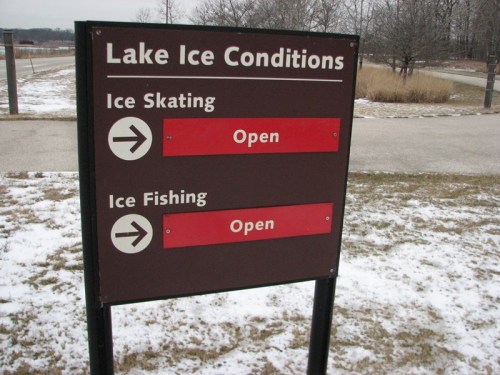 Sign indicating lake ice conditions: Ice Skating and Ice Fishing both marked as "Open." Snowy landscape in background.