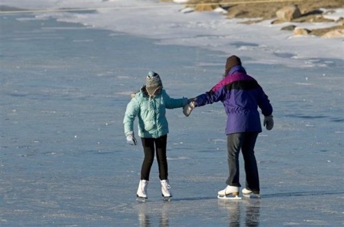 A child and an adult ice skating together on a frozen lake, holding hands and enjoying the winter day.