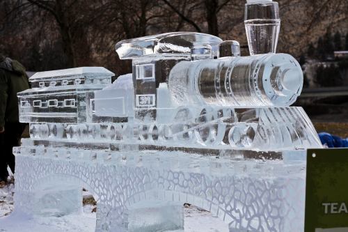 A detailed ice sculpture of a steam locomotive on a bridge, showcasing intricate carvings and a clear, icy finish.