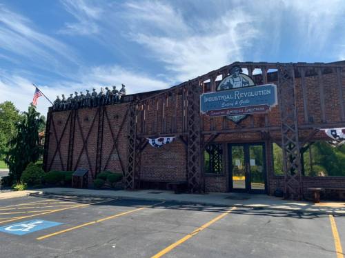 A brick building with a sign reading "Industrial Revolution" and a statue of soldiers on the roof, set against a blue sky.