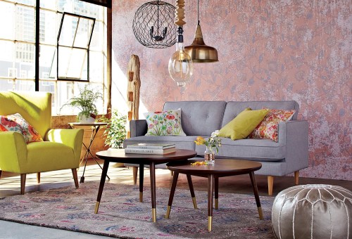 A stylish living room featuring a gray sofa, yellow armchair, wooden coffee tables, and decorative plants against a textured wall.