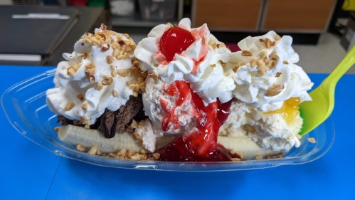 A banana split topped with whipped cream, nuts, chocolate and strawberry syrup, served in a clear dish.