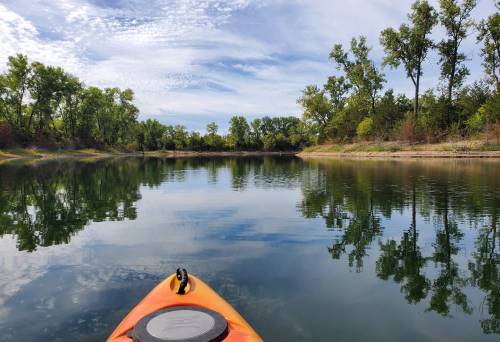 A kayak on calm water, surrounded by trees and reflecting clouds in a serene landscape.