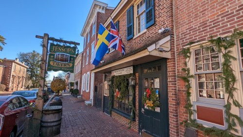 A charming brick tavern with festive decorations and flags, set in a quaint street lined with historic buildings.
