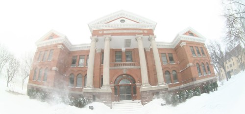 Historic brick building with columns, partially obscured by snow, under a cloudy winter sky.